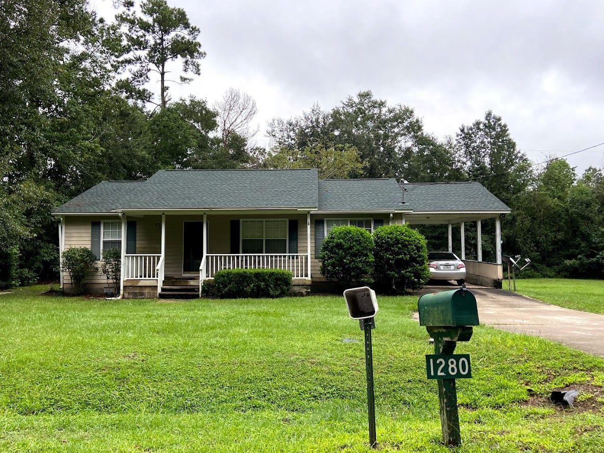 Single-story house with front porch and carport, surrounded by green lawn and trees; green mailbox with house number 1280 in the foreground.