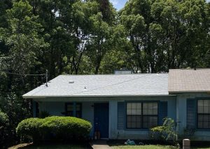 Roofers installing a new residential roof on a blue house in Tallahassee, Florida.