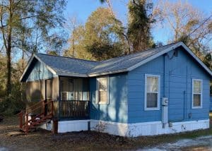 New roof installation on a blue house with a small porch and surrounding trees.