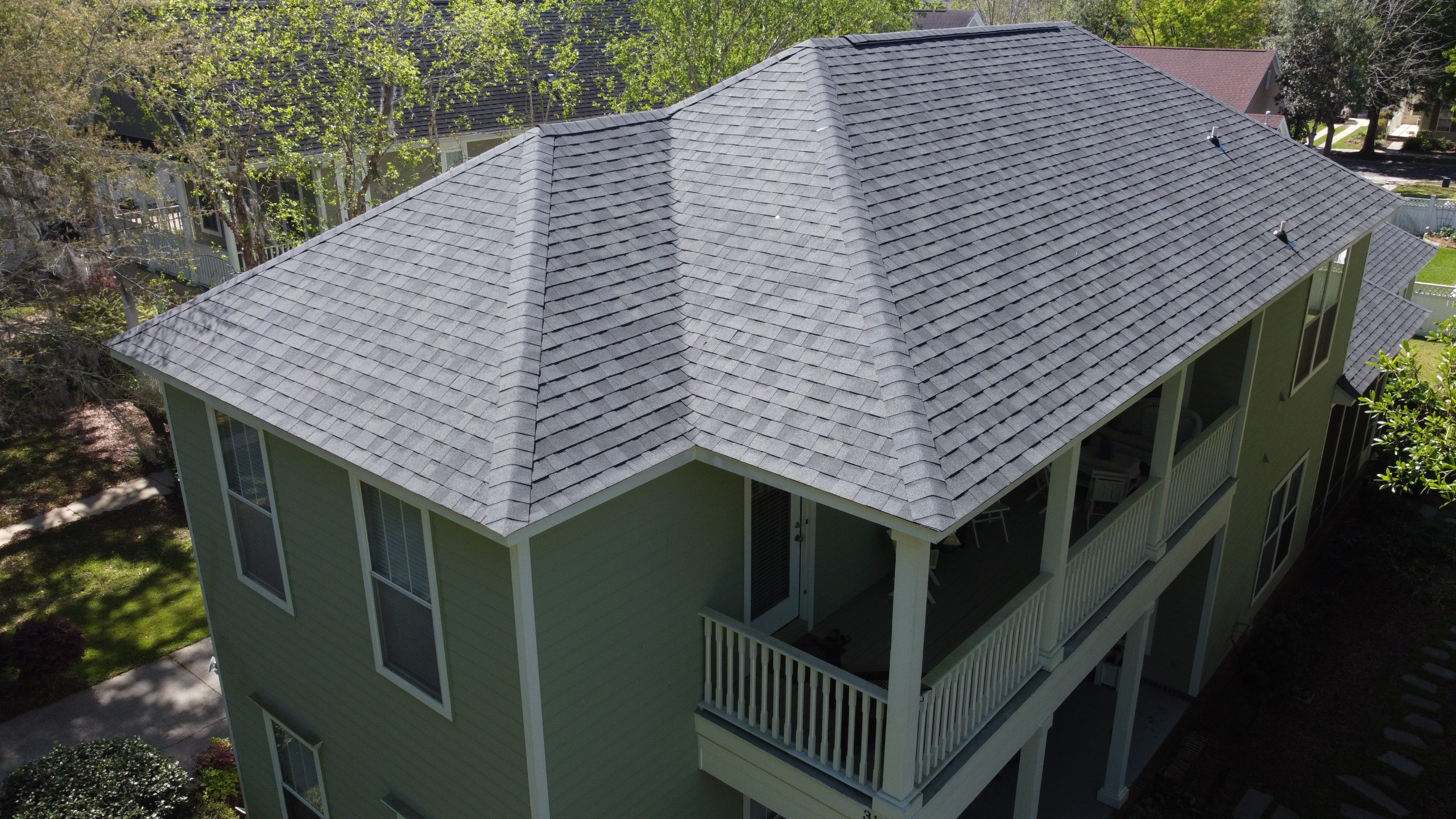 Aerial view of a two-story house with a gray shingle roof, green exterior walls, several windows, and a covered balcony.