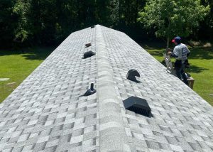 Roofers inspecting a new residential roof installation with vents and shingles.