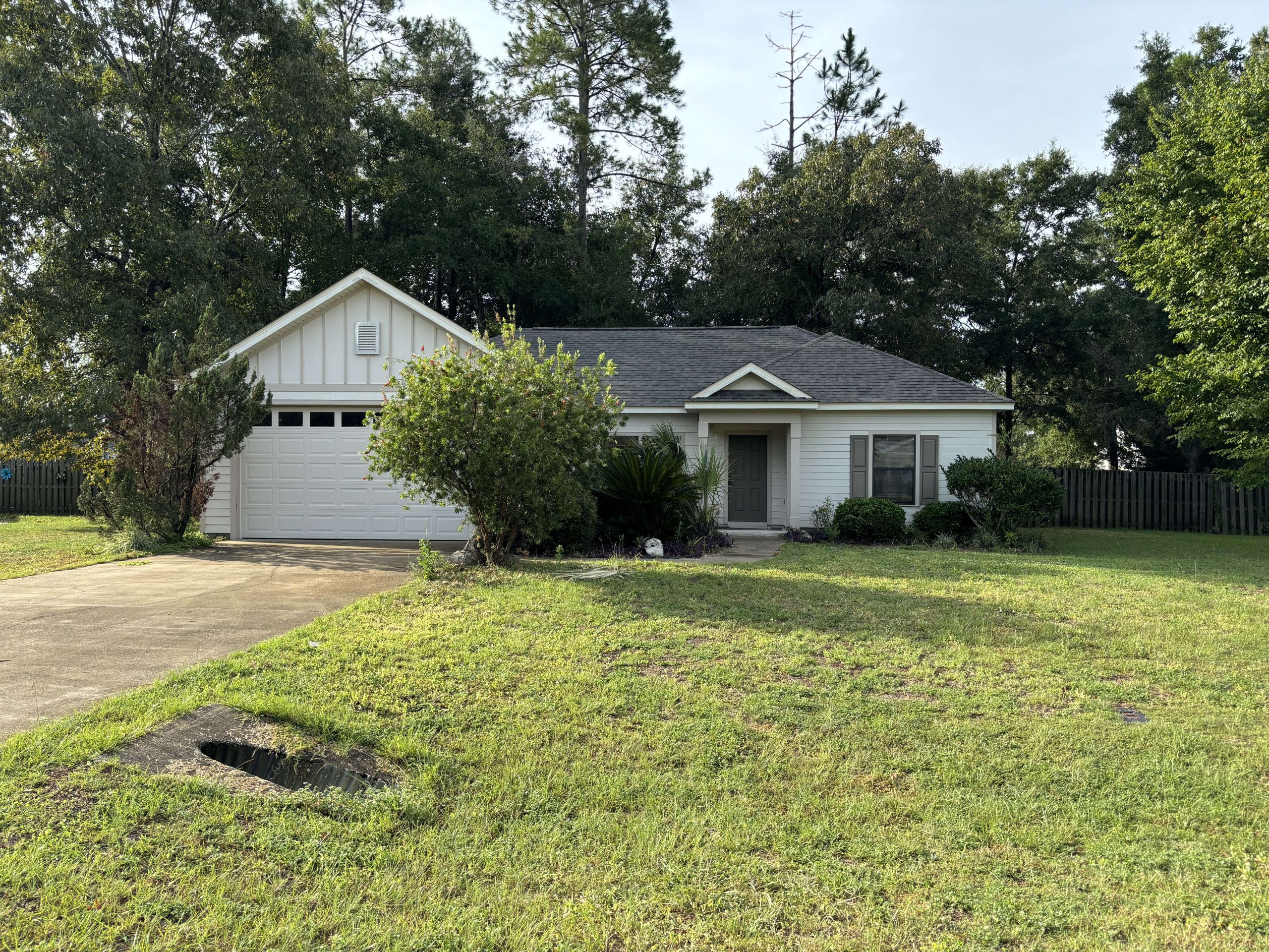 A single-story white house with a two-car garage, a gray roof, and a small porch, surrounded by trees and a grassy yard.