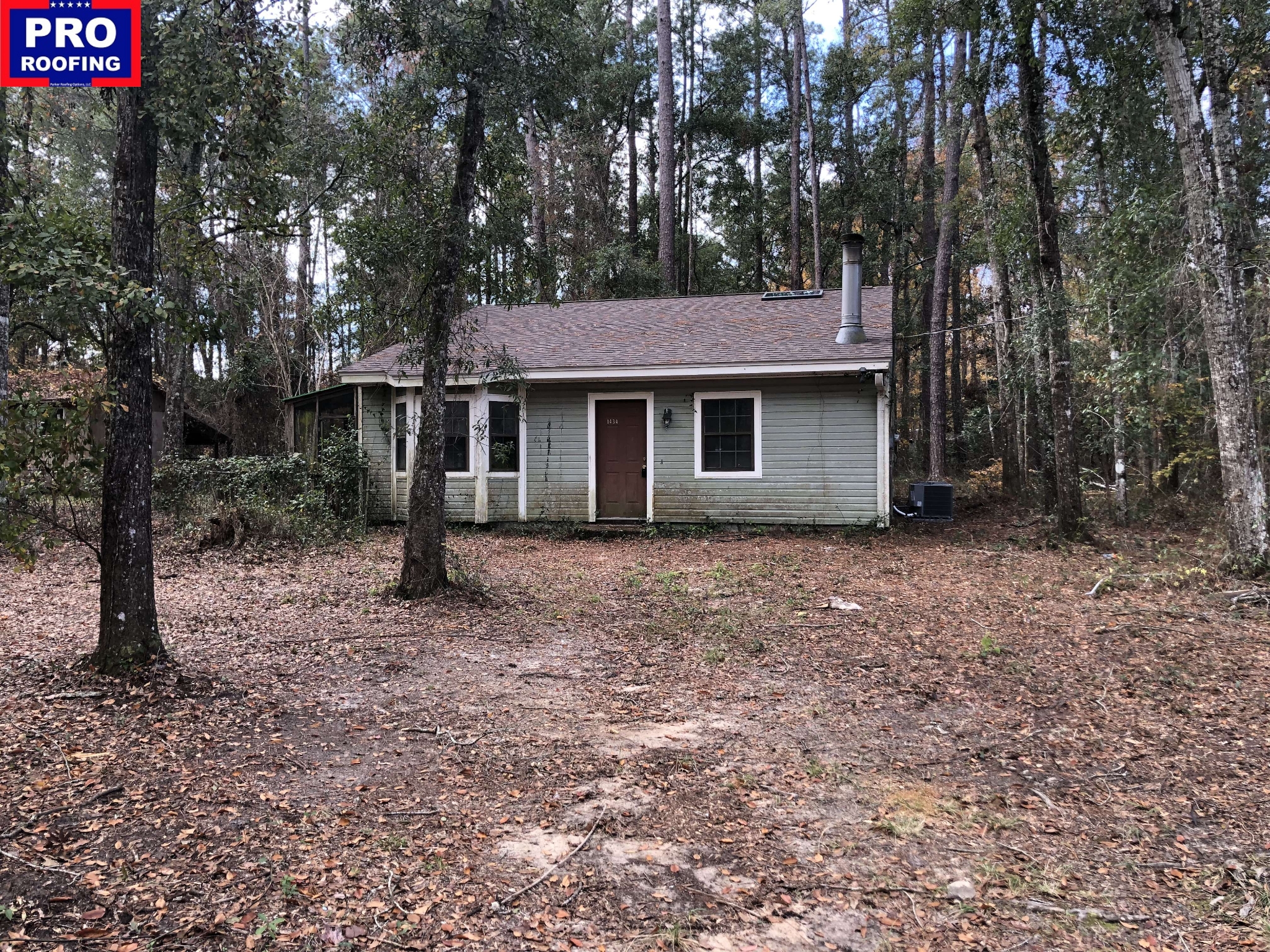 A small, single-story house with a shingle roof stands among tall trees; the lawn is covered with dry leaves. A Pro Roofing logo is displayed in the top left corner.